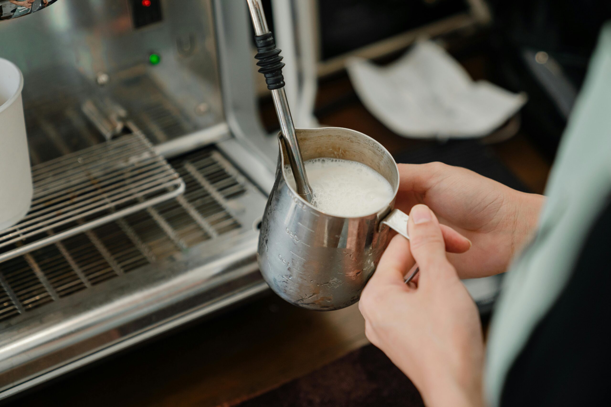 Close-up of barista steaming milk with an espresso machine in a café setting.